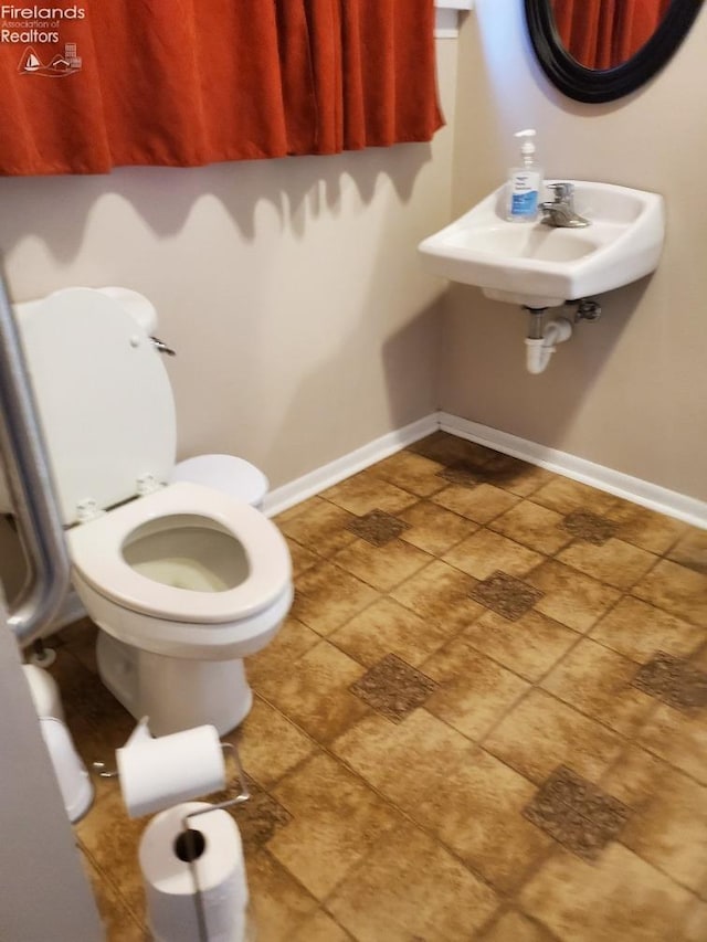 half bathroom featuring toilet, baseboards, and a sink