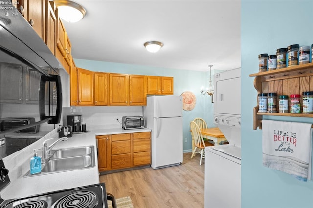 kitchen featuring stacked washer / dryer, light countertops, light wood-type flooring, freestanding refrigerator, and a sink