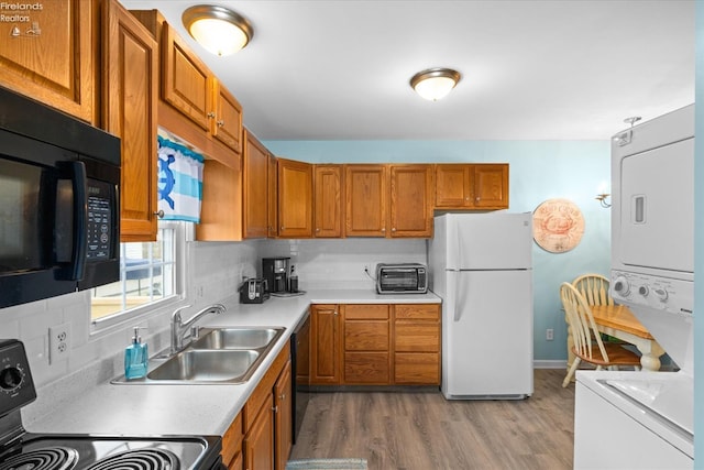 kitchen with brown cabinets, black appliances, stacked washing maching and dryer, and a sink