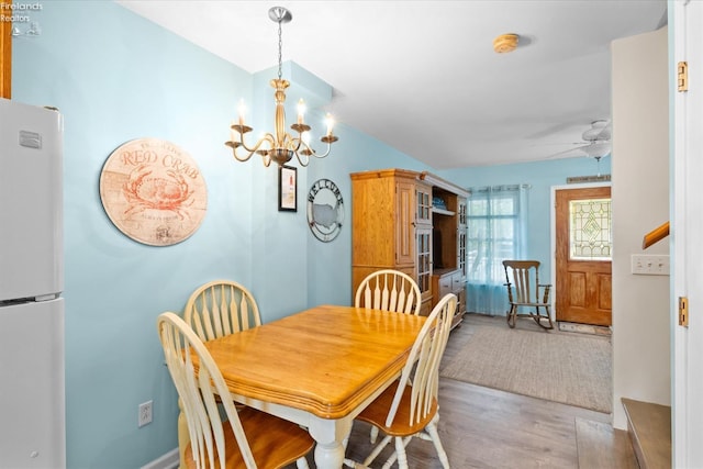 dining space with ceiling fan with notable chandelier, light wood-type flooring, and lofted ceiling