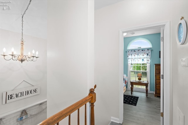 corridor featuring an upstairs landing, a notable chandelier, baseboards, and light wood-style floors