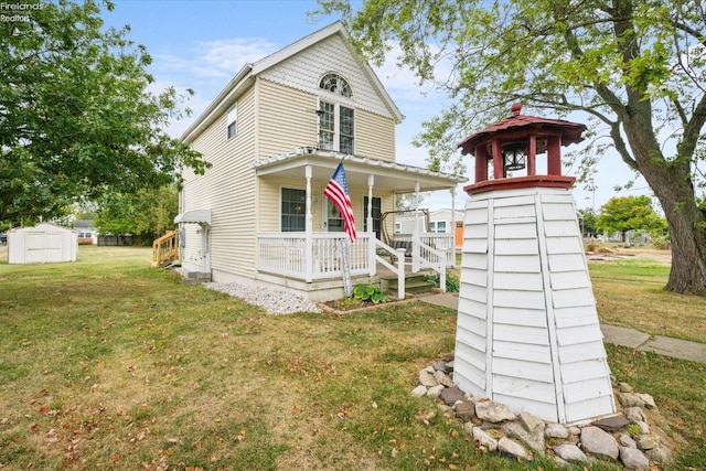 view of front of home featuring a front lawn, a storage unit, an outbuilding, and covered porch