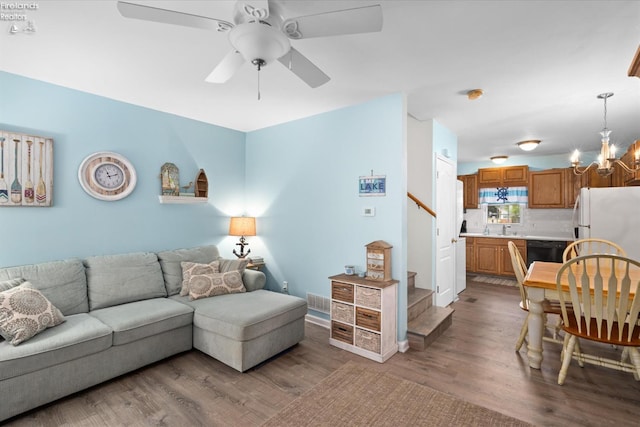 living area with ceiling fan with notable chandelier, stairway, and wood finished floors