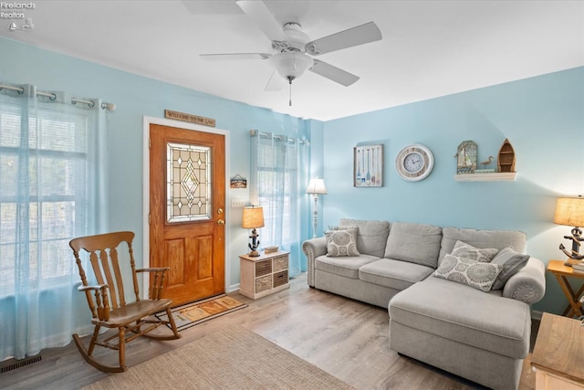 living room with a wealth of natural light, visible vents, wood finished floors, and ceiling fan