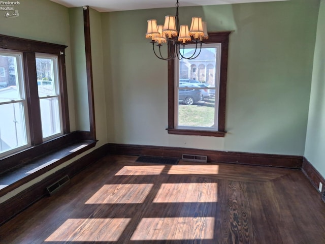 unfurnished dining area featuring baseboards, wood finished floors, visible vents, and a chandelier