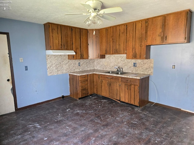 kitchen featuring backsplash, brown cabinetry, under cabinet range hood, and a sink