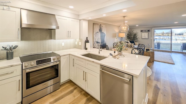 kitchen featuring open floor plan, white cabinetry, stainless steel appliances, a peninsula, and wall chimney range hood