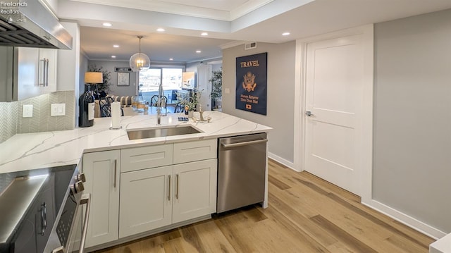 kitchen with a peninsula, ornamental molding, a sink, appliances with stainless steel finishes, and wall chimney exhaust hood