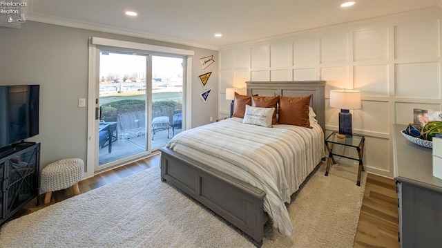 bedroom featuring wood finished floors, access to exterior, crown molding, and a decorative wall