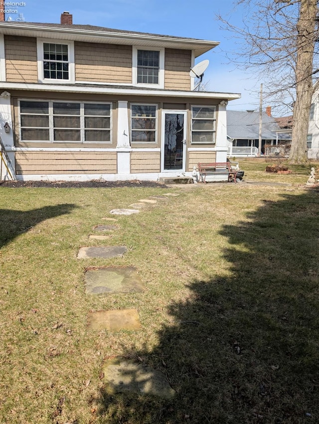 rear view of property featuring a lawn and a chimney