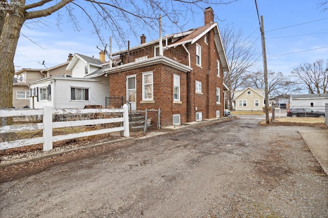 view of side of home featuring driveway, brick siding, a fenced front yard, and a chimney