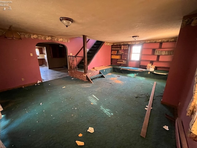 unfurnished living room with stairway, arched walkways, and a textured ceiling