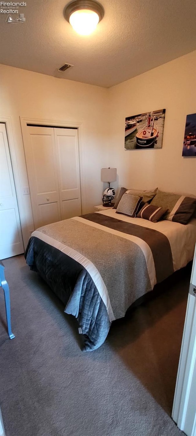 bedroom featuring visible vents, a textured ceiling, a closet, and dark carpet