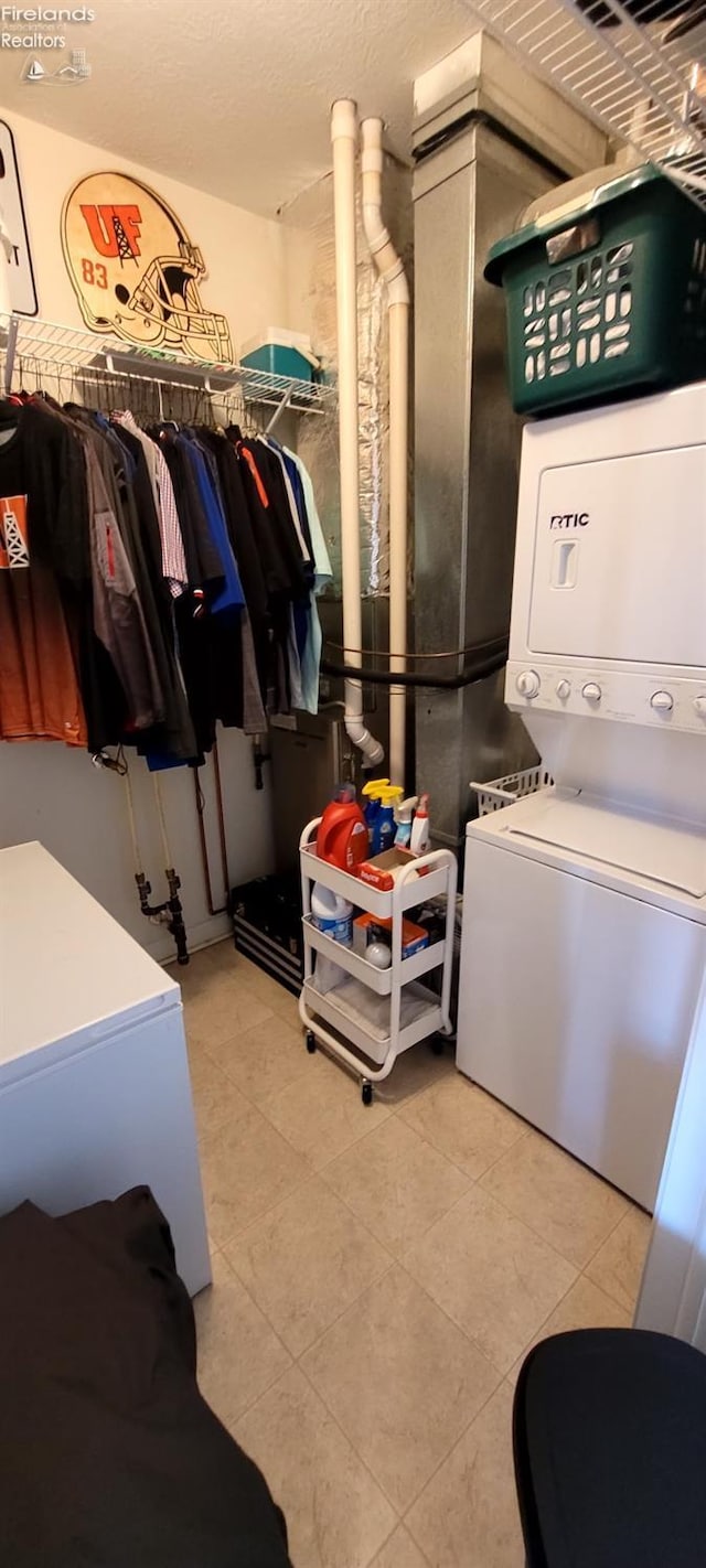 laundry area with laundry area, stacked washer and clothes dryer, tile patterned floors, and a textured ceiling