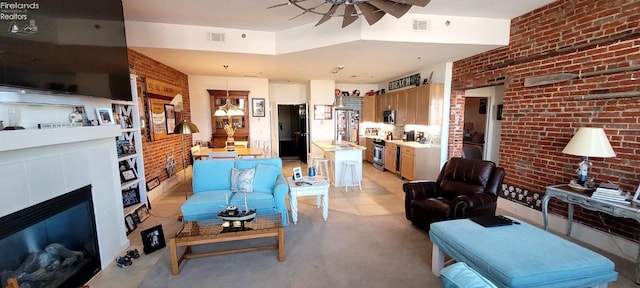 living room with a glass covered fireplace, a ceiling fan, visible vents, and brick wall