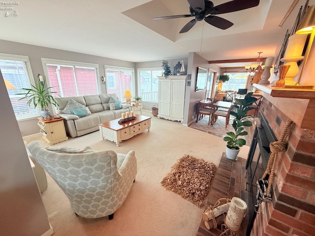 living area with carpet flooring, ceiling fan with notable chandelier, a brick fireplace, and baseboards