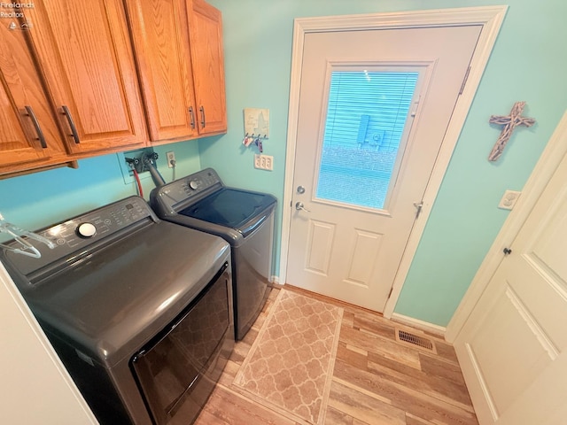 clothes washing area featuring visible vents, baseboards, washer and clothes dryer, light wood-style floors, and cabinet space