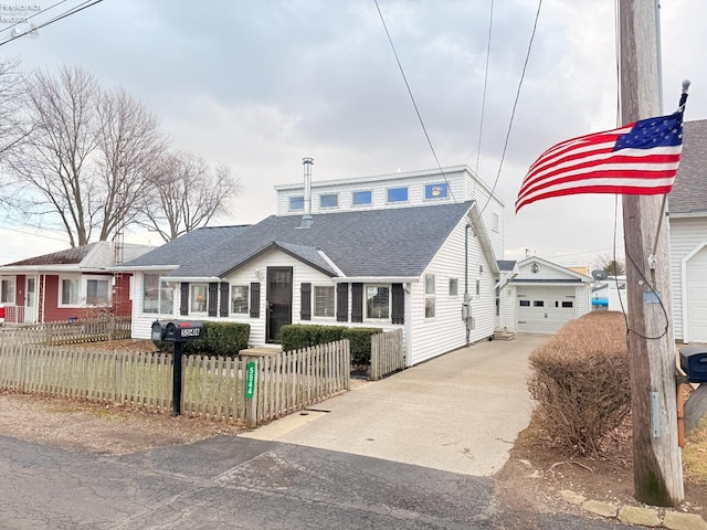 view of front of house with roof with shingles, an outdoor structure, concrete driveway, a garage, and a fenced front yard