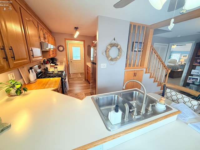 kitchen featuring a ceiling fan, a sink, under cabinet range hood, appliances with stainless steel finishes, and brown cabinets