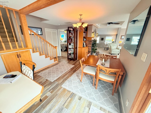 living area with visible vents, baseboards, light wood-type flooring, stairs, and ceiling fan with notable chandelier