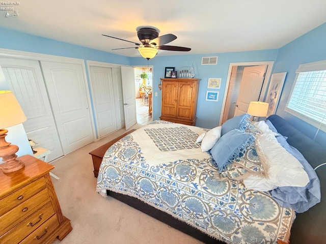 bedroom featuring visible vents, carpet flooring, two closets, and a ceiling fan