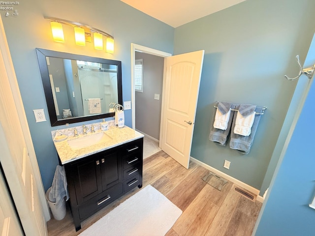 bathroom with visible vents, baseboards, wood finished floors, vanity, and a shower