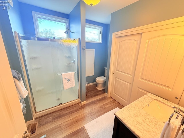 bathroom with visible vents, toilet, a stall shower, wood finished floors, and vanity