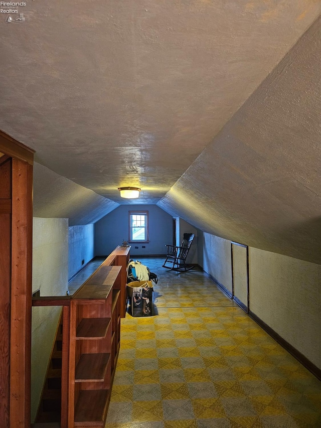 additional living space with tile patterned floors, a textured ceiling, baseboards, and vaulted ceiling