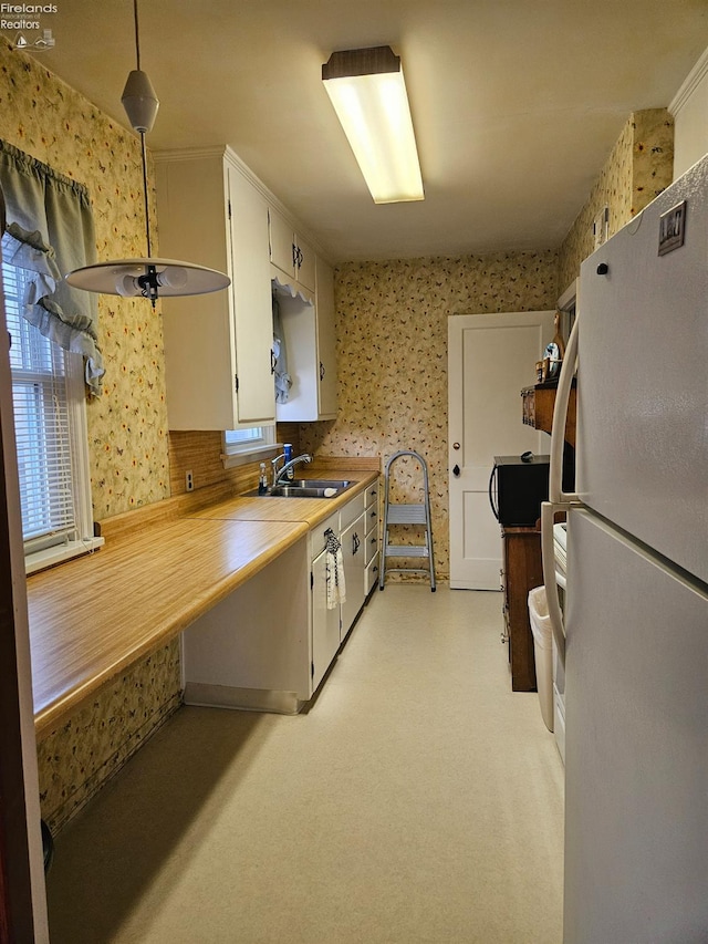 kitchen with white cabinetry, wallpapered walls, freestanding refrigerator, and a sink