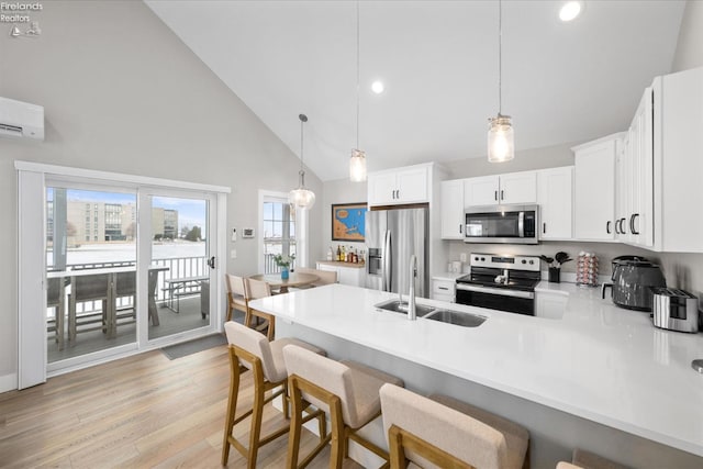 kitchen featuring light wood finished floors, a peninsula, stainless steel appliances, white cabinetry, and a sink