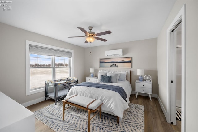 bedroom with a ceiling fan, a wall mounted AC, baseboards, and wood finished floors