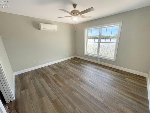 spare room with an AC wall unit, wood finished floors, baseboards, and ceiling fan