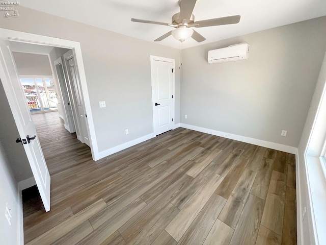 unfurnished bedroom with a ceiling fan, wood finished floors, baseboards, and a wall mounted air conditioner