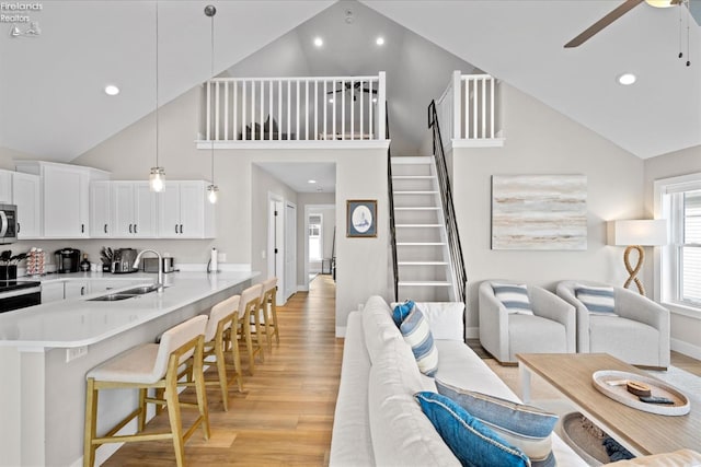 interior space featuring light wood finished floors, ceiling fan, a kitchen bar, white cabinets, and a sink