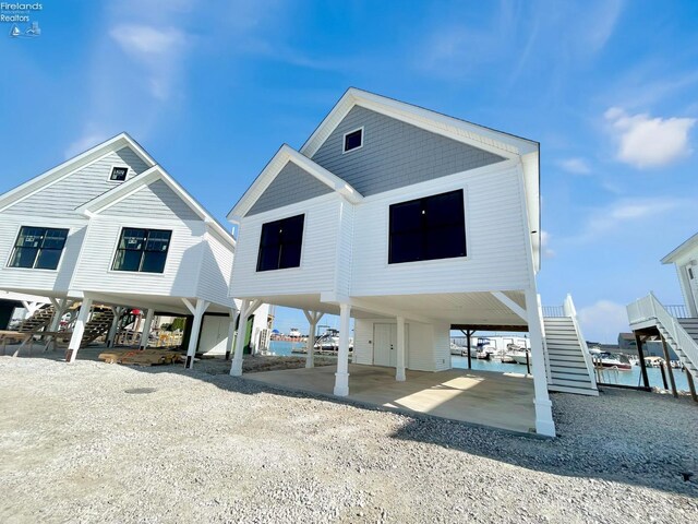 coastal home with dirt driveway, a carport, and stairs