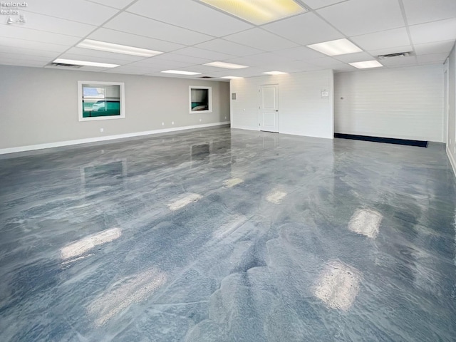 empty room with concrete flooring, visible vents, baseboards, and a drop ceiling