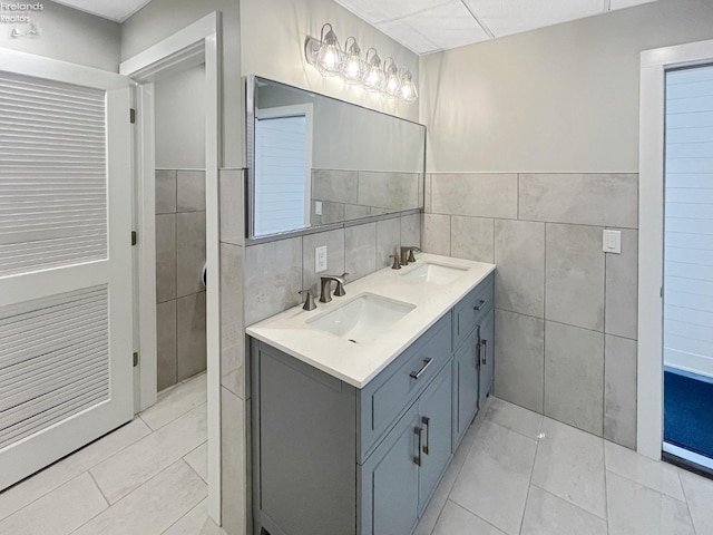 full bathroom with a sink, tile walls, and double vanity