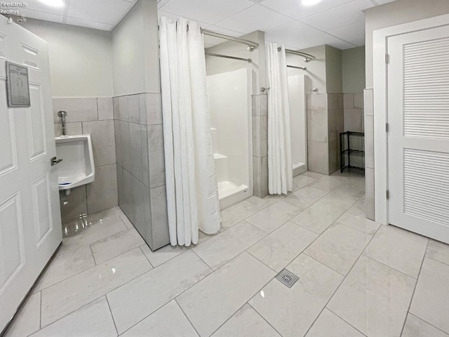 bathroom featuring a drop ceiling, tile walls, wainscoting, and a shower stall