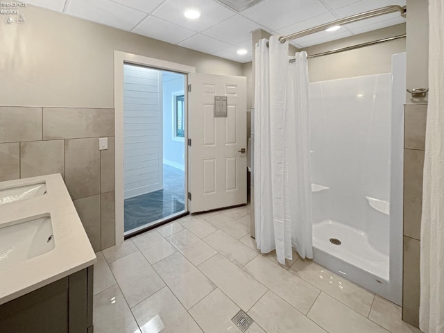 full bathroom with a drop ceiling, a shower stall, tile walls, and a sink