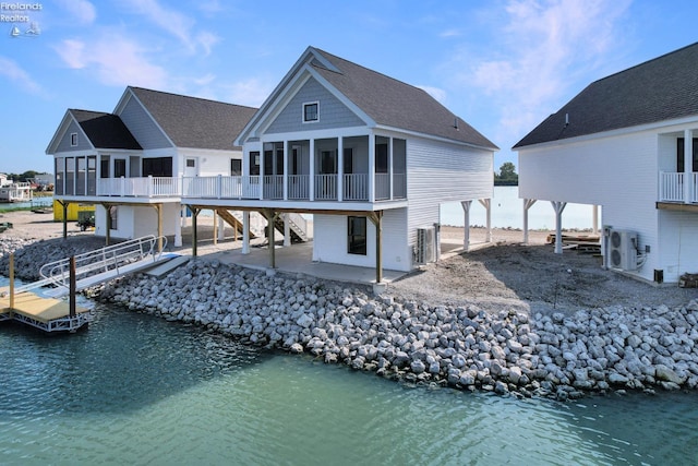 back of house featuring a water view, a patio, roof with shingles, a sunroom, and stairs