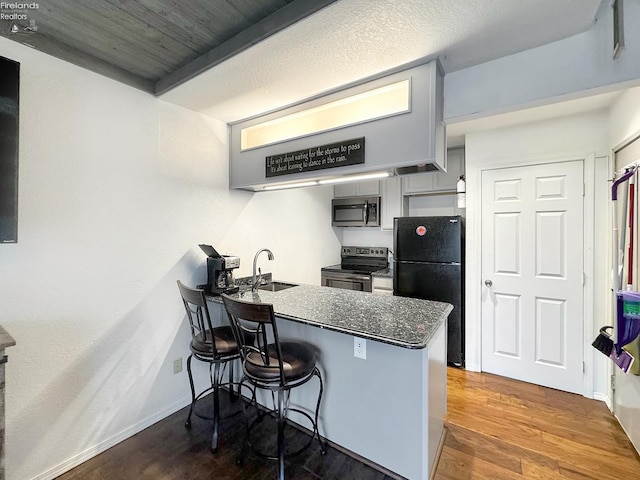 kitchen with a sink, a kitchen breakfast bar, wood finished floors, stainless steel appliances, and a peninsula