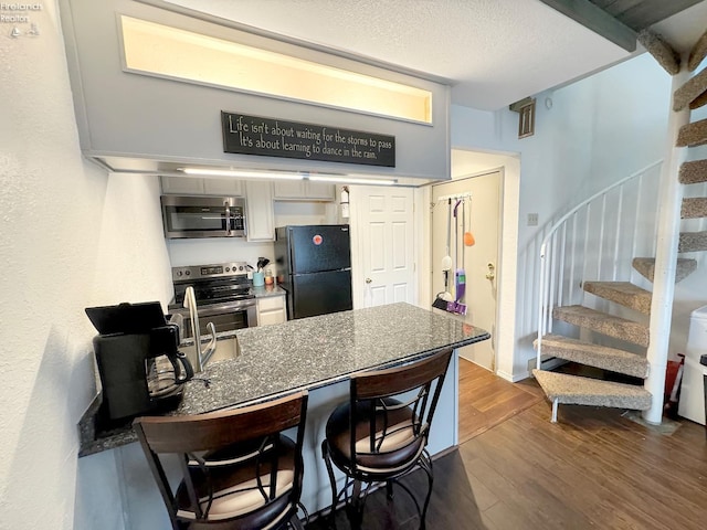 kitchen with dark wood-type flooring, a breakfast bar, a textured ceiling, white cabinetry, and appliances with stainless steel finishes