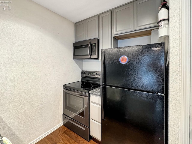 kitchen with baseboards, gray cabinetry, dark wood-type flooring, appliances with stainless steel finishes, and a textured wall