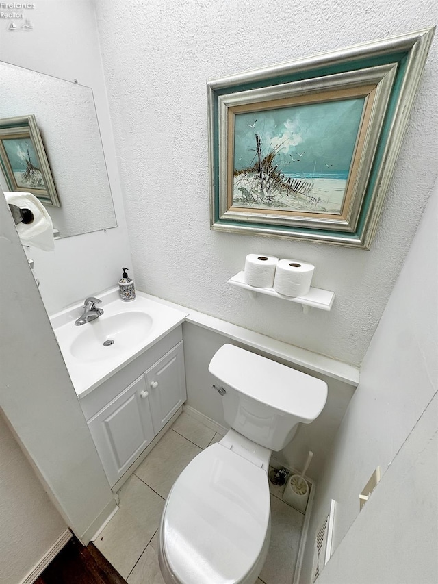 half bathroom with tile patterned floors, toilet, vanity, and a textured wall