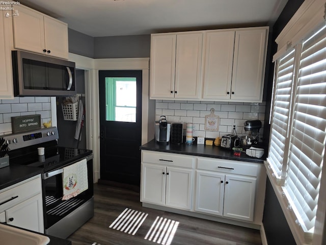 kitchen with dark wood finished floors, appliances with stainless steel finishes, white cabinetry, dark countertops, and backsplash