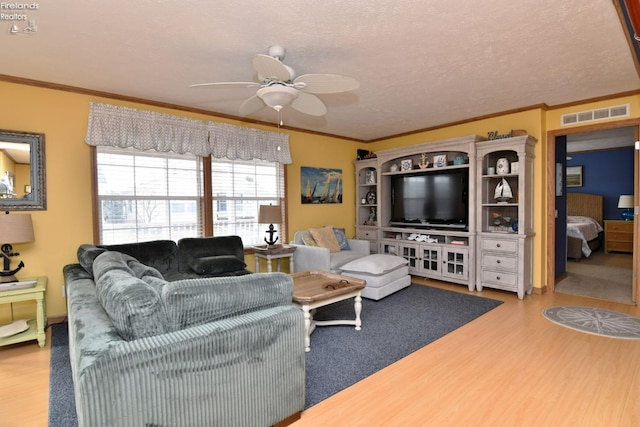 living area with visible vents, ornamental molding, a textured ceiling, wood finished floors, and ceiling fan