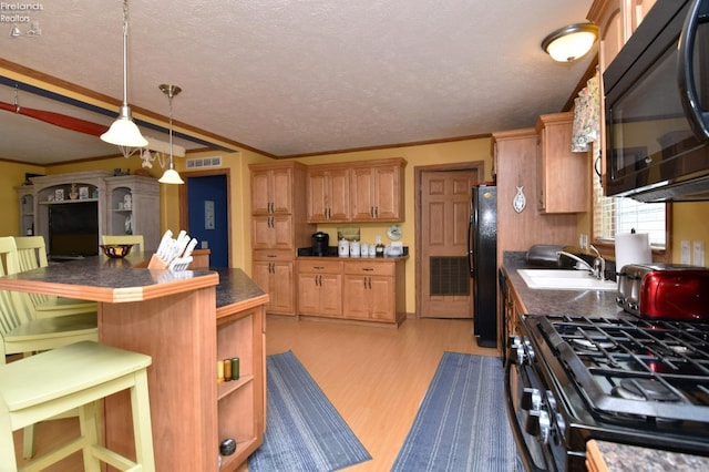 kitchen featuring a breakfast bar area, a sink, black appliances, light wood-style floors, and dark countertops