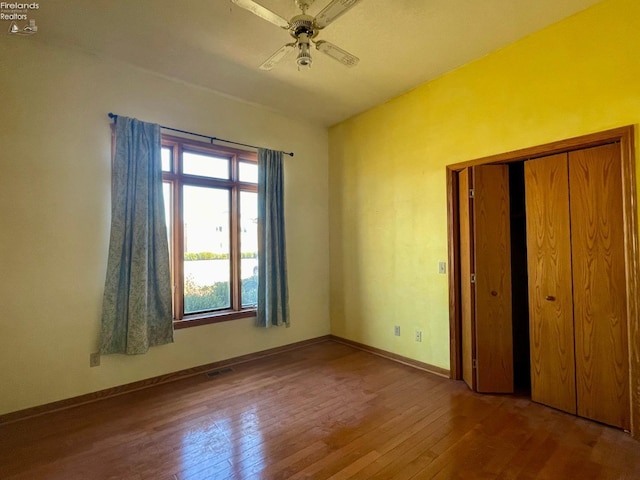 unfurnished bedroom with hardwood / wood-style floors, baseboards, visible vents, ceiling fan, and a closet