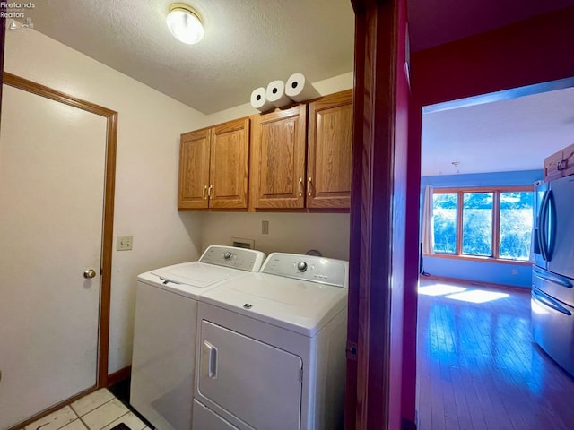 washroom with baseboards, light wood-style flooring, cabinet space, a textured ceiling, and independent washer and dryer