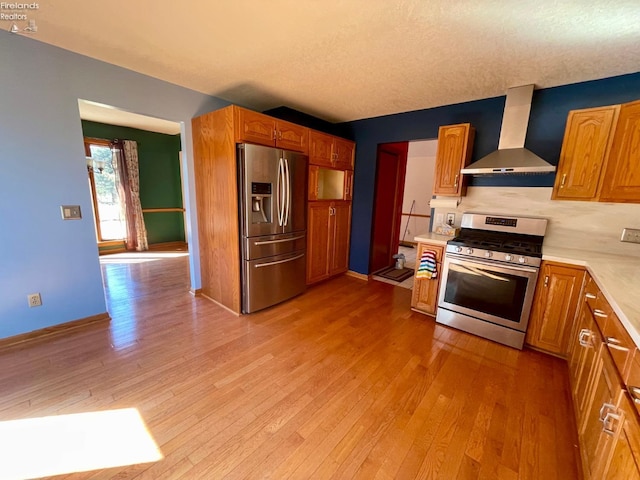 kitchen featuring light countertops, wall chimney range hood, light wood finished floors, and stainless steel appliances